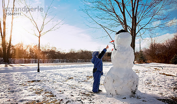 Kleiner Junge zeigt auf Schneemann an sonnigem Tag