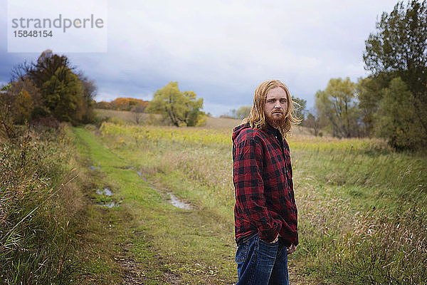 Junger Mann mit langen roten Haaren und Bart draußen auf dem Land