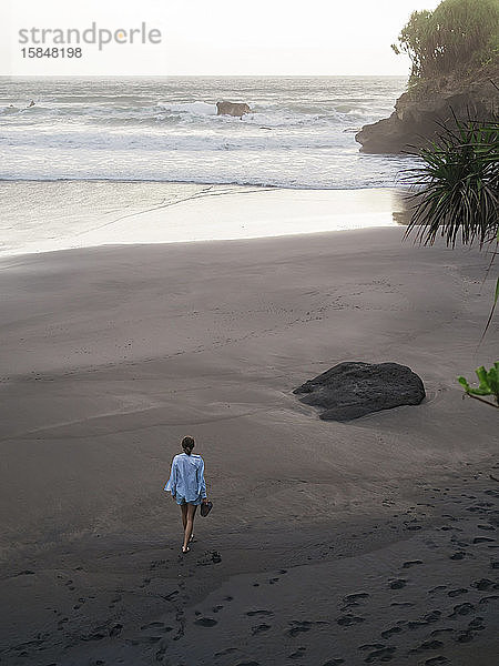 Junge Frau  die an einem felsigen Strand spazieren geht und die Aussicht betrachtet