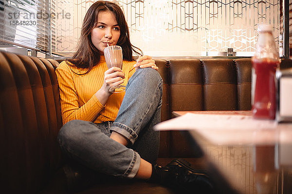 Nachdenkliches Teenager-Mädchen trinkt Schokoladenmilchshake im Restaurant