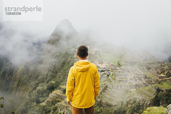 Ein Mann in gelber Jacke steht in der Nähe der Ruinen von Machu Picchu  Peru