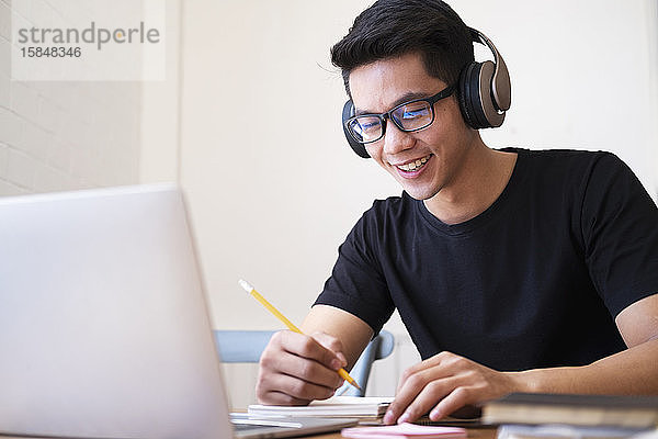 Junger Mann studiert zu Hause mit Laptop und lernt online