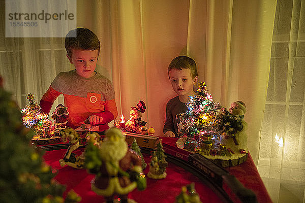 Zwei Brüder schauen während der Feiertage der Modelleisenbahn beim Weihnachtsschmuck zu