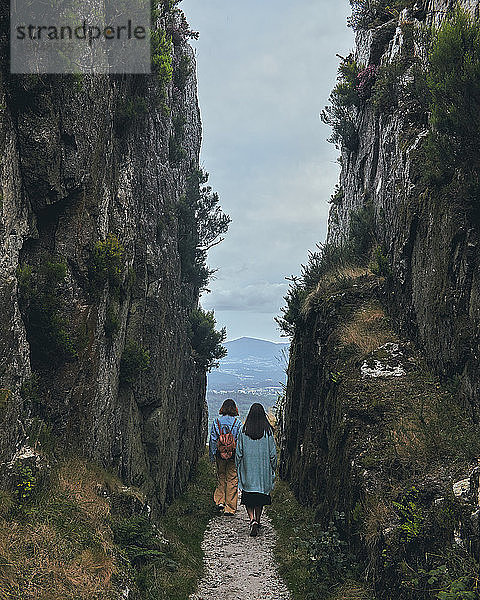 Zwei junge Frauen gehen durch einen Pfad zwischen Bergen bewölkter Tag