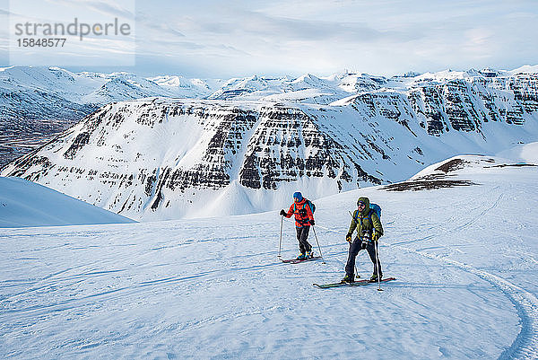 Mann und Frau beim Skifahren in Island mit Bergen im Hintergrund