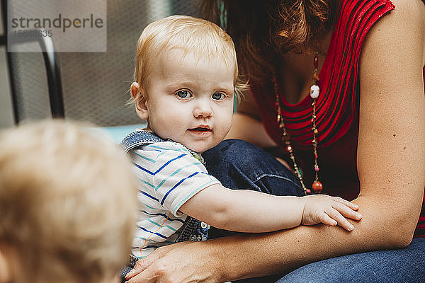 Süßer Junge hält sich an den Armen der Mutter