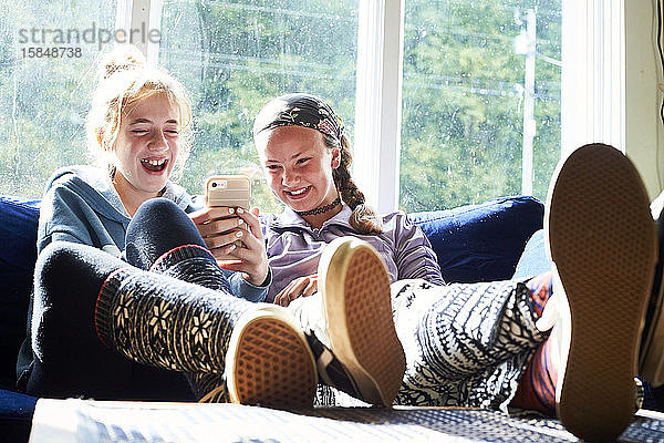 Teenager-Mädchen  die auf einer Couch lachen und etwas am Telefon anschauen