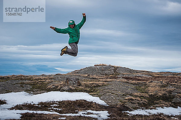 Mann in Jacke springt vom Felsen in Akureyri  Island