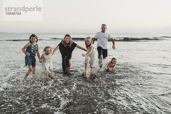 Familie mit vier Mädchen  die bei Sonnenuntergang spielen und in Wellen planschen