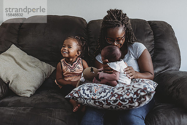 Multirassische Familie auf dem Sofa  während die Mutter das Kind neben dem lächelnden Mädchen hält