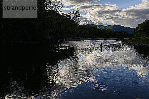 Ein einsamer Mann in einem Fluss beim Angeln bei Sonnenuntergang.