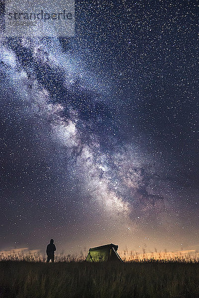 Silhouette eines Bergsteigers  der neben dem Zelt steht und die Sterne beobachtet