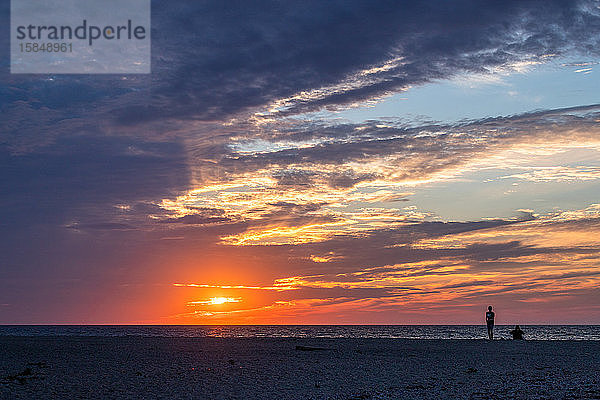 Ein Paar  das einen wunderschönen Sonnenuntergang am Strand beobachtet.