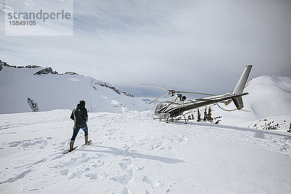Abenteuerlustige Frau mit Schneeschuhen in Richtung Hubschrauber.