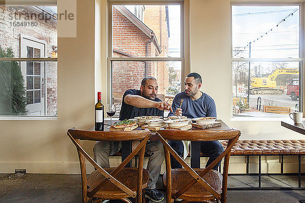 Zwei Männer teilen sich eine Mahlzeit und eine Flasche Wein in einem leeren Restaurant