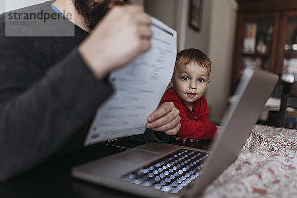 Nahaufnahme eines kleinen Sohnes  der sich den Computer seines Vaters ansieht  während er zu Hause arbeitet