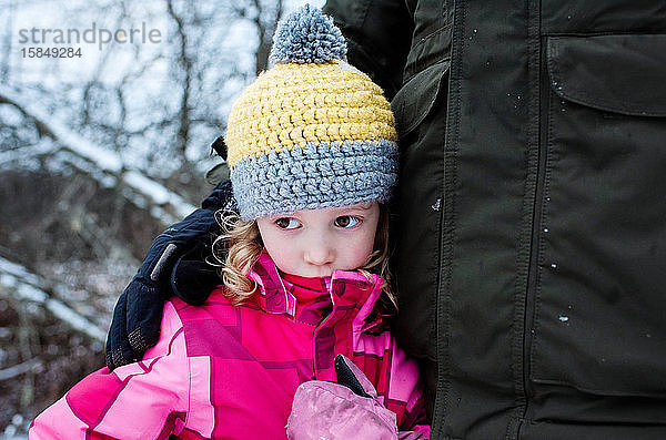 junges Mädchen sieht traurig aus und kuschelt mit ihrem Vater  während sie draußen im Schnee spielt