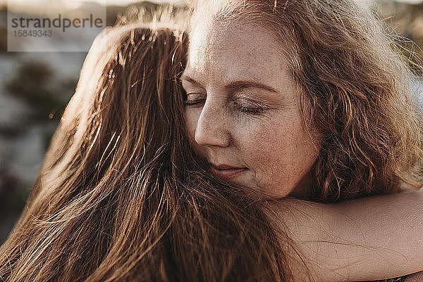 Detailaufnahme des Gesichts einer Mutter  die ihre Tochter am Strand umarmt