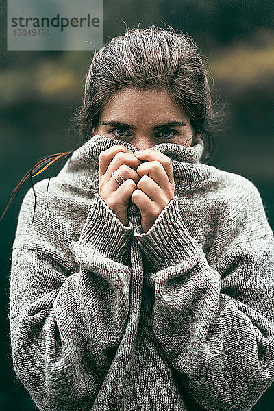 Porträt einer jungen Frau  die ihr Gesicht mit einem bequemen Pullover bedeckt