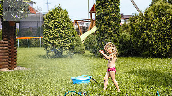 Kleines Mädchen spielt mit Wasser im Hof des Hauses