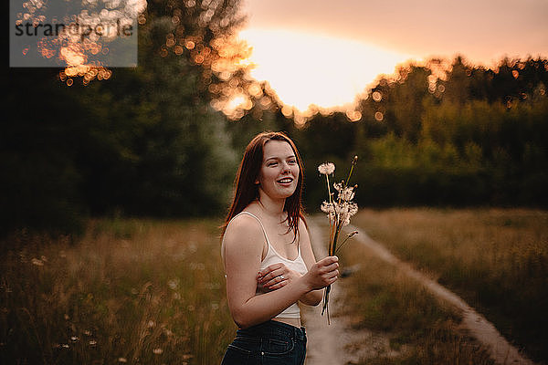 Glückliche junge Frau hält bei Sonnenuntergang einen Strauss Löwenzahnblumen