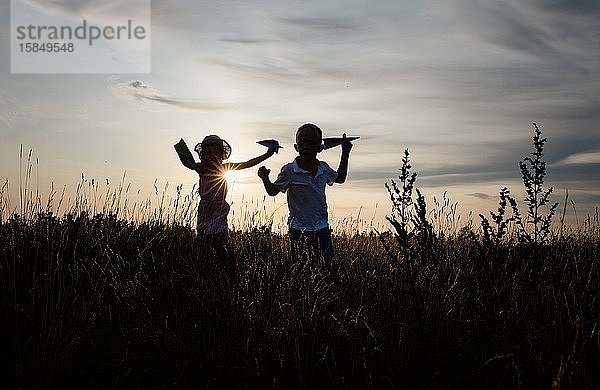 Geschwister  die im Sommer bei Sonnenuntergang draußen auf einer Wiese spielen