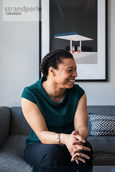 Lächelnde selbstbewusste Unternehmerin sitzt im Büro auf dem Sofa an der Wand