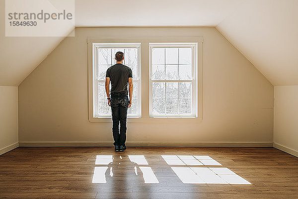 Mann steht vor einem Innenfenster in einem leeren  einsamen  minimalistischen Raum