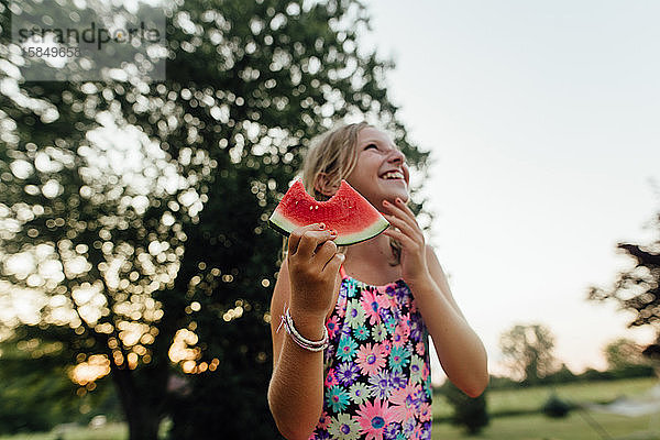 Junges Mädchen mit großem Lächeln isst im Sommer draußen Wassermelone