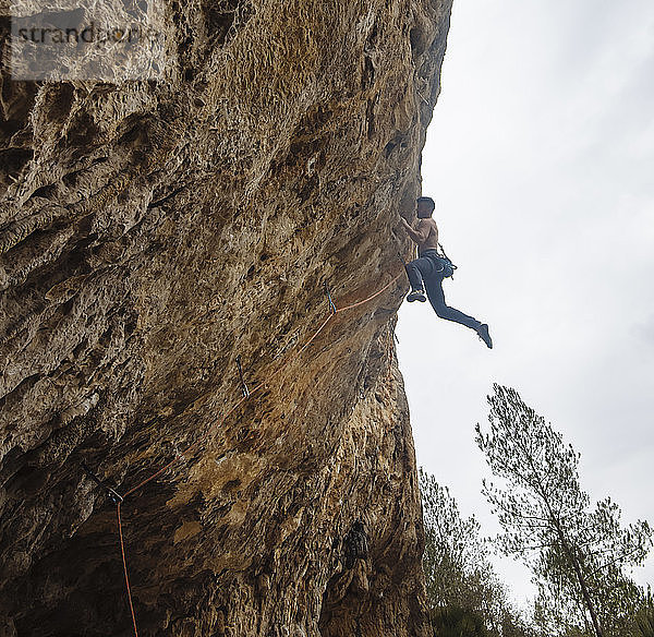 Ein Bergsteiger ohne Hemd schickt eine Sportkletterroute am spanischen Fels.