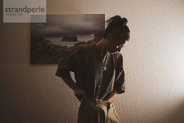 Androgyne Frau steckt nachts ihr Hemd vor einem Kunstwerk zu Hause in die Hose
