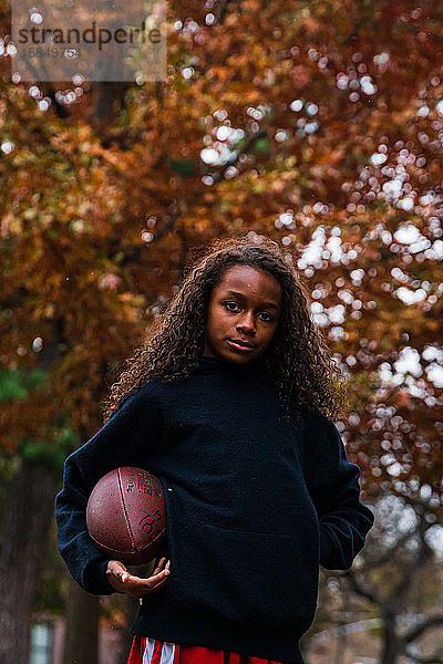 Porträt eines selbstbewussten Mädchens  das American Football im Park hält