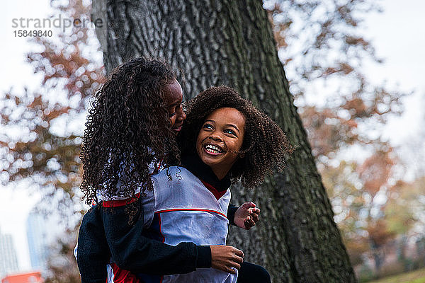 Fröhliches Mädchen mit Huckepack-Schwester im Park