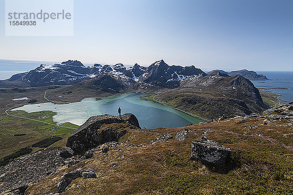 Weibliche Wanderin mit Blick auf das farbenprächtige Wasser des Flakstadpollen und die umliegende Berglandschaft  FlakstadÃ¸y  Lofoten-Inseln  Norwegen