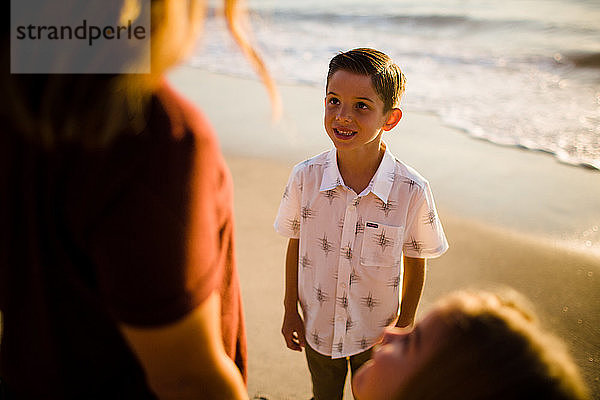 Sohn lächelt Mutter an  während er bei Sonnenuntergang am Strand steht