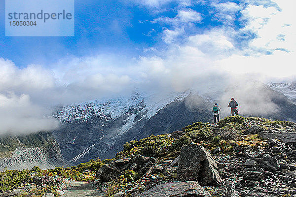 Wanderer  die umgeben von Gletscherbergen in den Wolken Ausblicke nehmen.