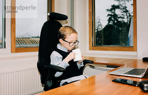 Junge Junge trinkt Kaffee im Büro seines Vaters bei der Arbeit