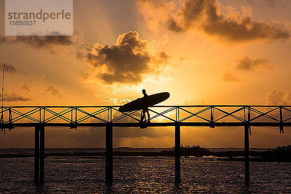 Silhouette eines Mannes mit einem Surfbrett auf der Brücke der Wolke neun