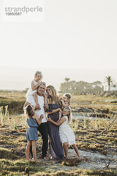 Lifestyle-Porträt einer Familie mit jungen Mädchen  die bei Sonnenuntergang am Strand lächeln