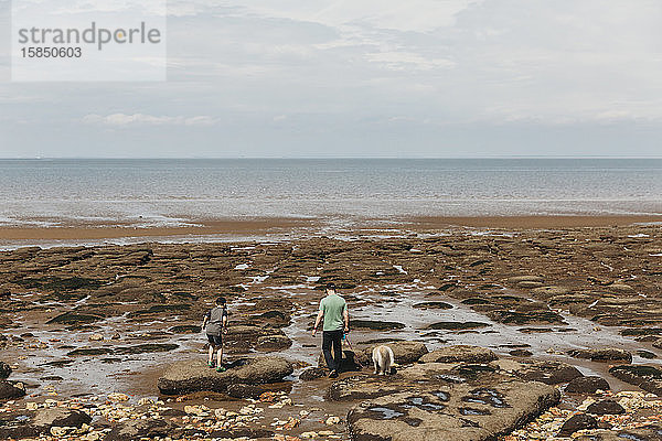 Vater  Sohn und Hund gehen über Felsen in Richtung Meer