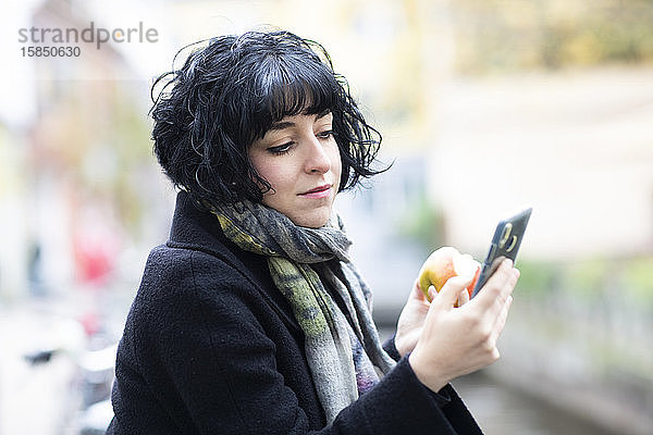 junge Frau mit Apfel und Smartphone draußen