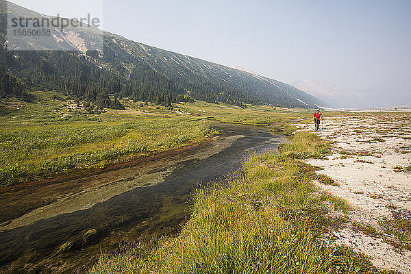 Wanderer  der im Alpental am Bach entlang wandert.