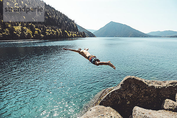 Seitenansicht eines jungen Mannes beim Springen im Alpensee vor den Bergen