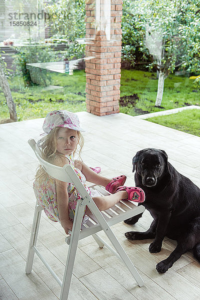 Ein kleines Mädchen sitzt auf dem Hof mit einem großen Labrador-Retriever-Hund