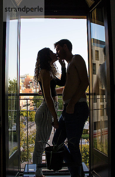 Zu Hause küssendes Paar  das bei geöffnetem Fenster im Rahmen steht