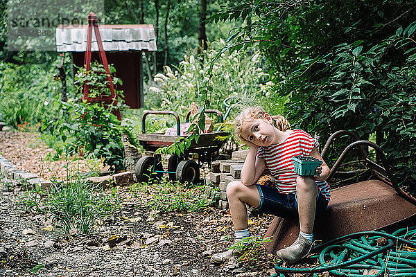 Ein kleines Mädchen sitzt auf einem Bauernhof mit frisch gepflückten Blaubeeren