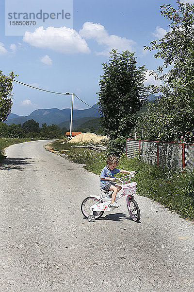 Ein kleiner Junge fährt Fahrrad auf einer leeren Straße in den Bergen