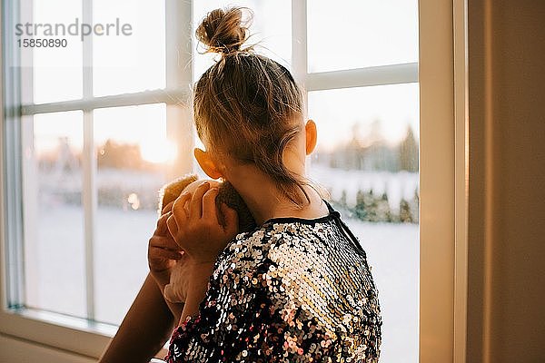 Mädchen  das in einem funkelnden Kleid aus dem Fenster schaut und den Sonnenuntergang beobachtet