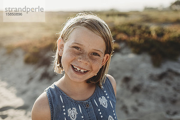 Porträt eines jungen Mädchens im Schulalter mit Sommersprossen lächelnd am Strand