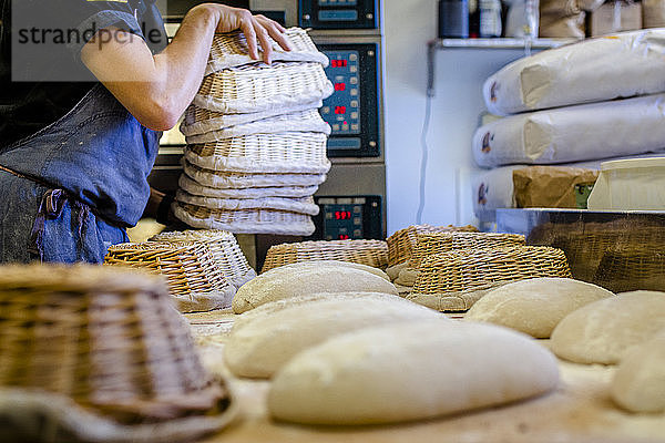 Ein professioneller Bäcker mit einem Stapel von Körben legt Brot auf die Theke